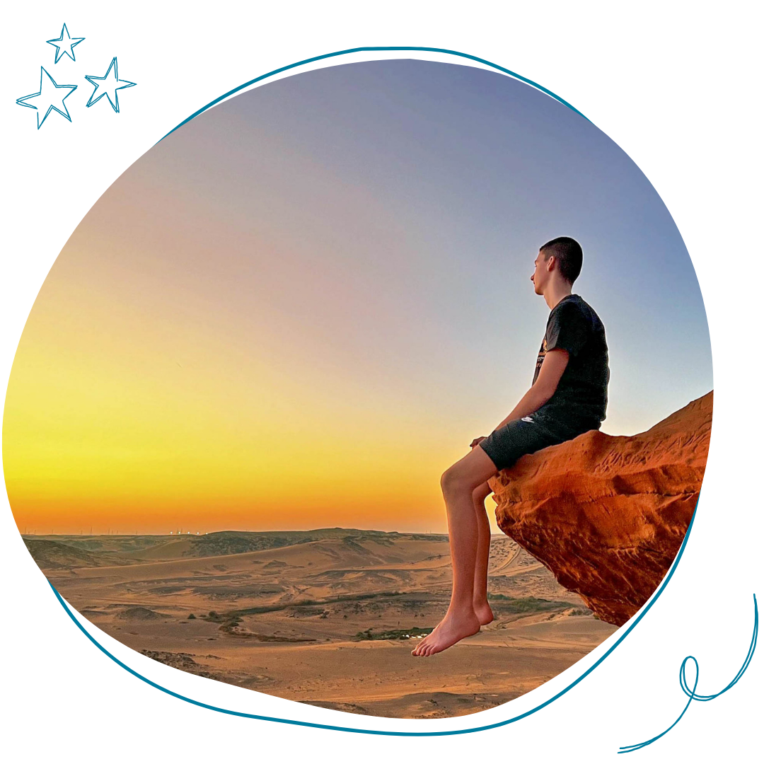 jeune homme assis sur un rocher devant un panorama au coucher du soleil