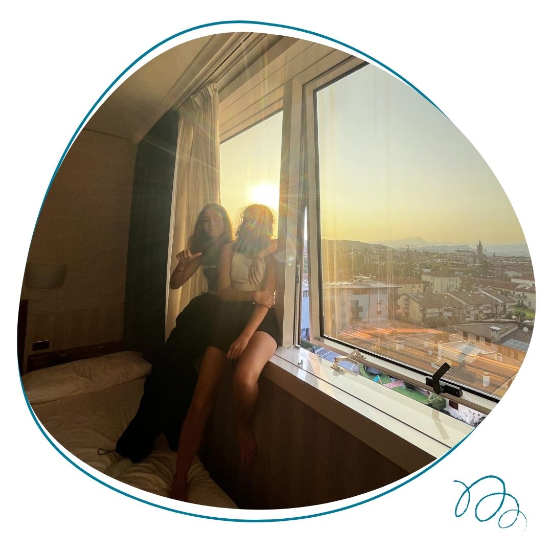 deux jeunes filles assises sur la fenetre de leur chambre d'hotel durant une colonie de vacances zigotours avec vue sur la ville derriere